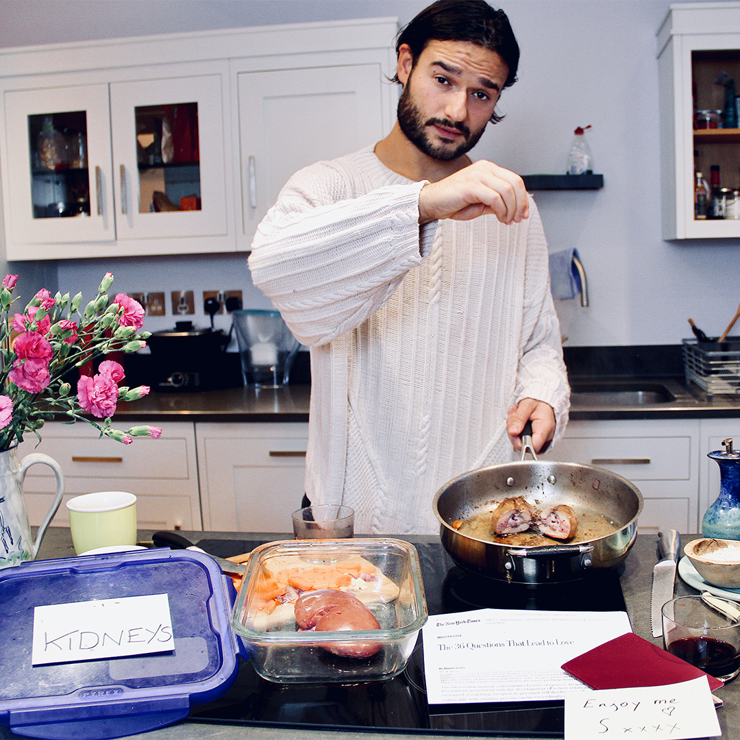 A young man with dark hair and a beard sprinkling salt over a pan with a piece of meat. Next to the pan is a box labeled 