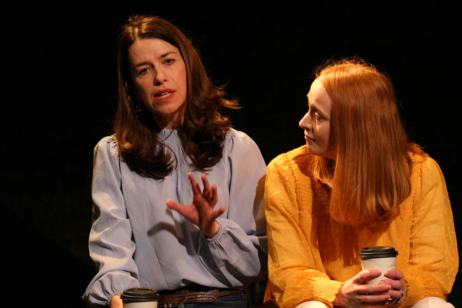 Two women sitting side by side holding coffee cups and having a conversation.