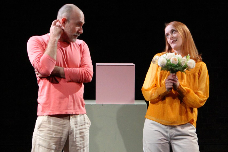 A caucasian man and woman standing next to eachother, the man scratching his head and the woman holding a boquet of flowers glancing over at the man.