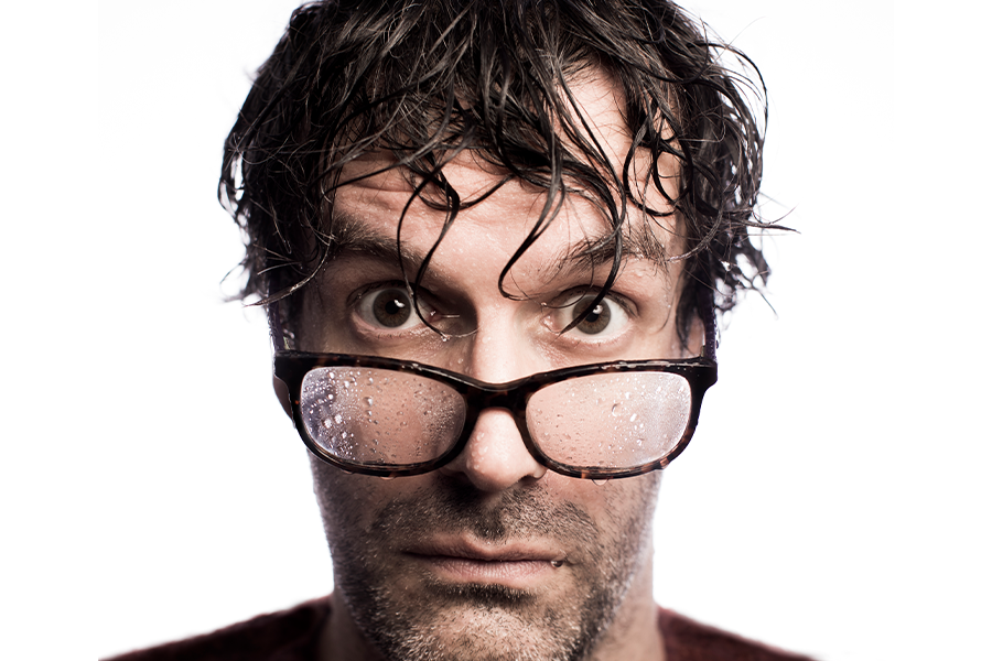A close-up of a caucasian man (Marcus Brigstocke) with his hair and glasses wet staring wide-eyed directly into the camera