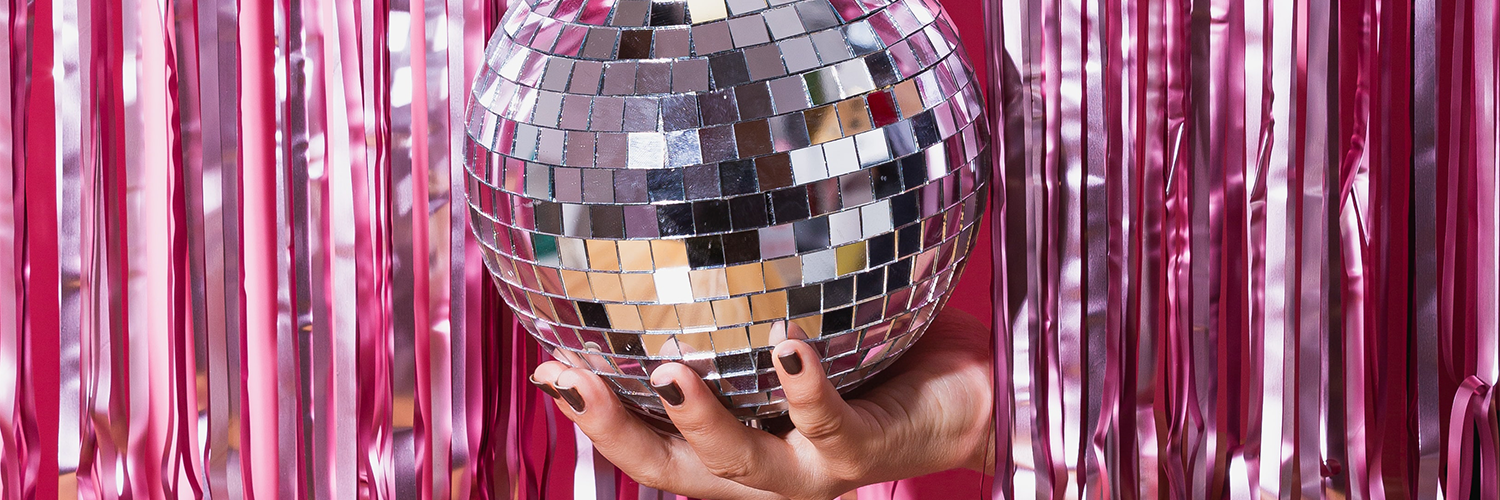 A hand with nail polish holding a discoball through a shiny pink foil fringe curtain