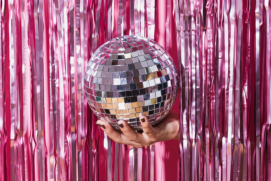 A hand with nail polish holding a discoball through a shiny pink foil fringe curtain