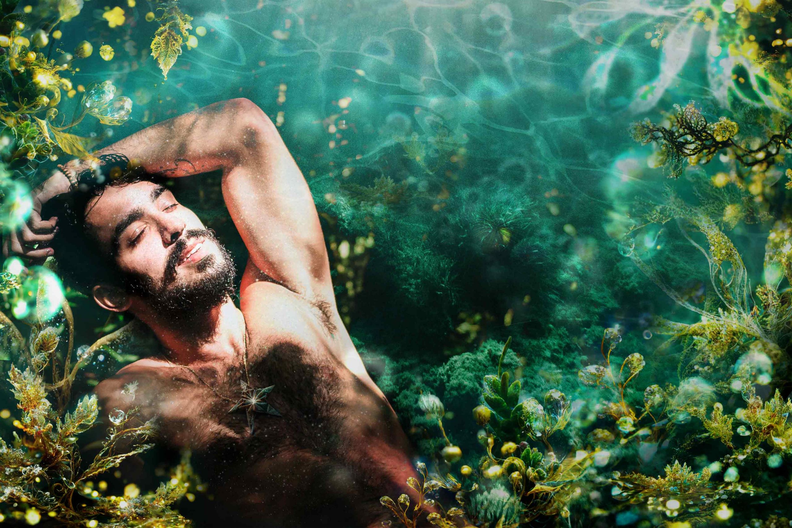 A bearded man lies back in sunlight, immersed in a fairytale-inspired, under the sea background with a starfish necklace on his exposed chest