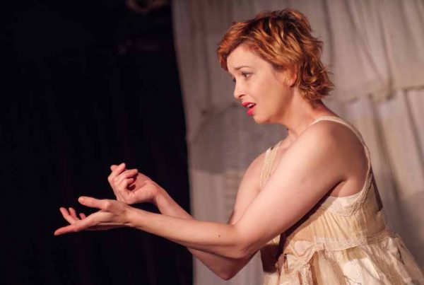 Portuguese theatre maker Marta Carvalho on stage in a white dress with hands outstretched.