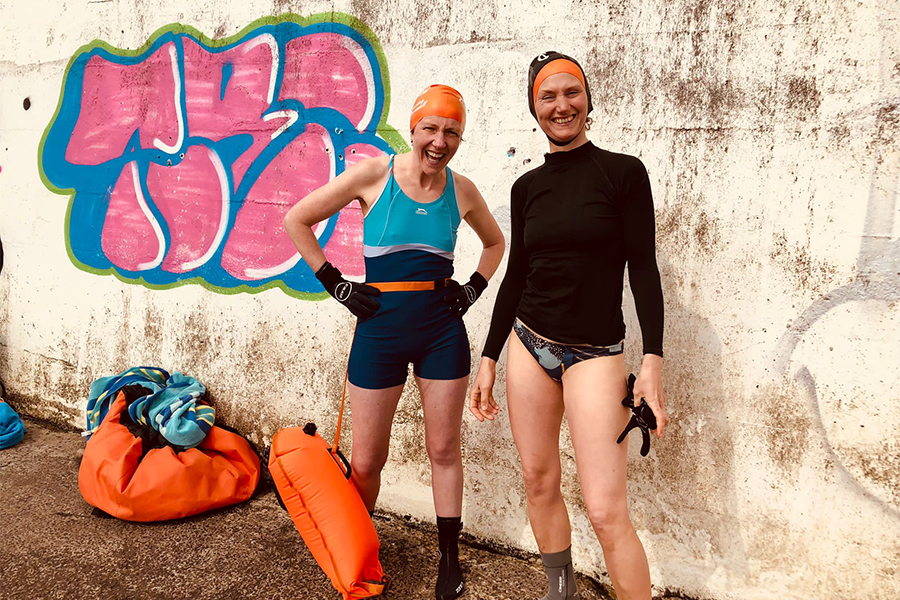 A photo of two people in outdoor swimming gear near a concrete graffitied wall