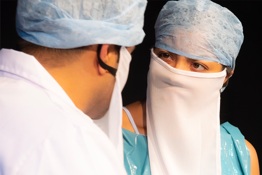 Two people in the medical field wearing scrubs, a hair net and a long white face mask