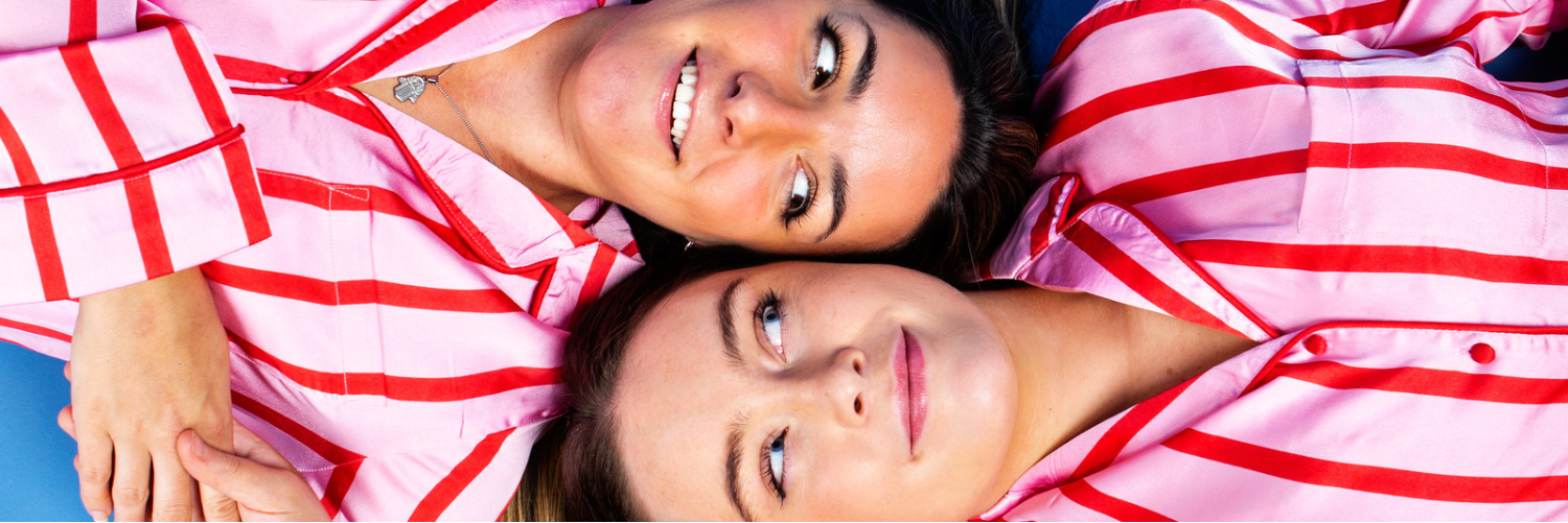 Two women lying down in opposite directions with their heads next to each other wearing pink and red striped pyjamas. Lead image of Mr Sister.