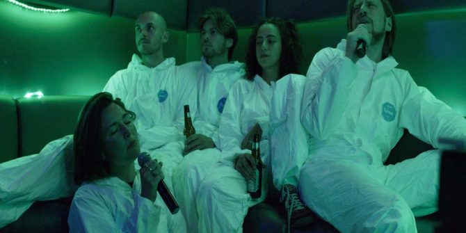 Five people sat in a karaoke booth wearing hazmat suits dimly lit in green