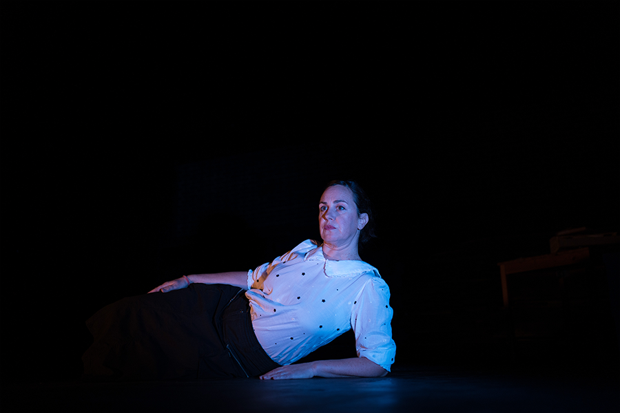 A woman lays sideways on the stage lit in red and blue