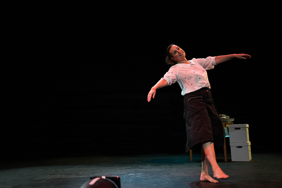 A woman dancing across the stage barefooted wearing a white blouse and a black midi length skirt