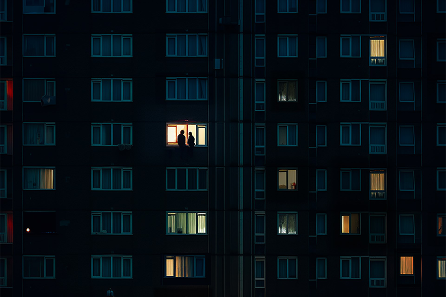 One window is lit amongst other closed curtains in a high-rise flat showing the silhouettes of two people