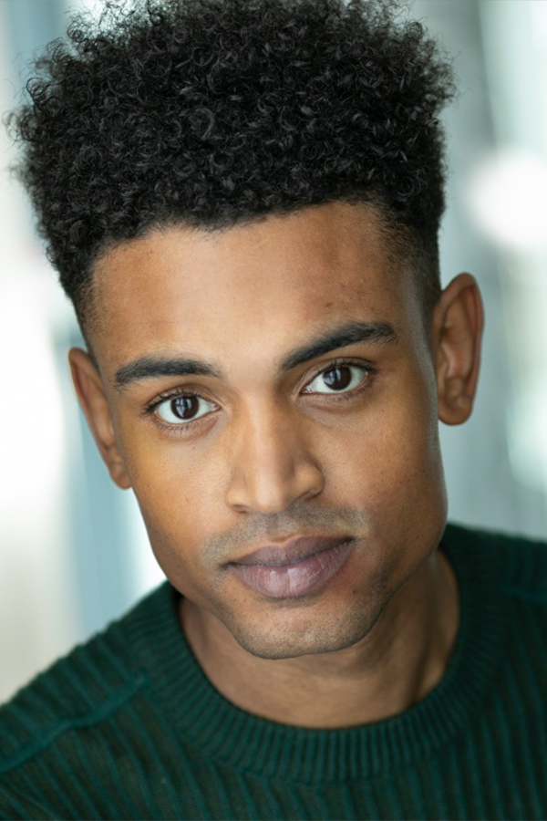 Headshot of Tré Medley, a black young man in his 20s. He is wearing a green cable knit jumper.