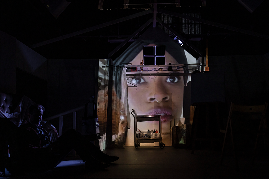 A woman's face is projected onto set wall.