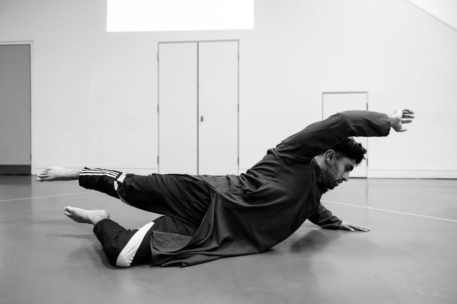 A black and white image of a man. He is on the floor of an empty hall. His limbs are outstretched.
