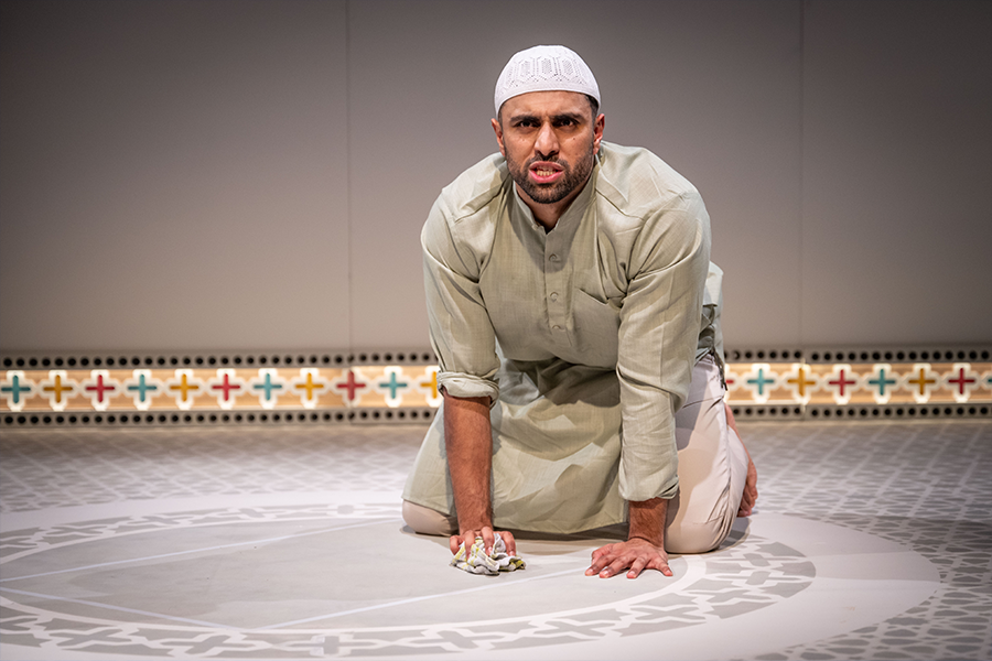 Azan Ahmed, a young south asian man, wears a Kurta and a Taqiyah. He is cleaning the floor on his hands and knees.
