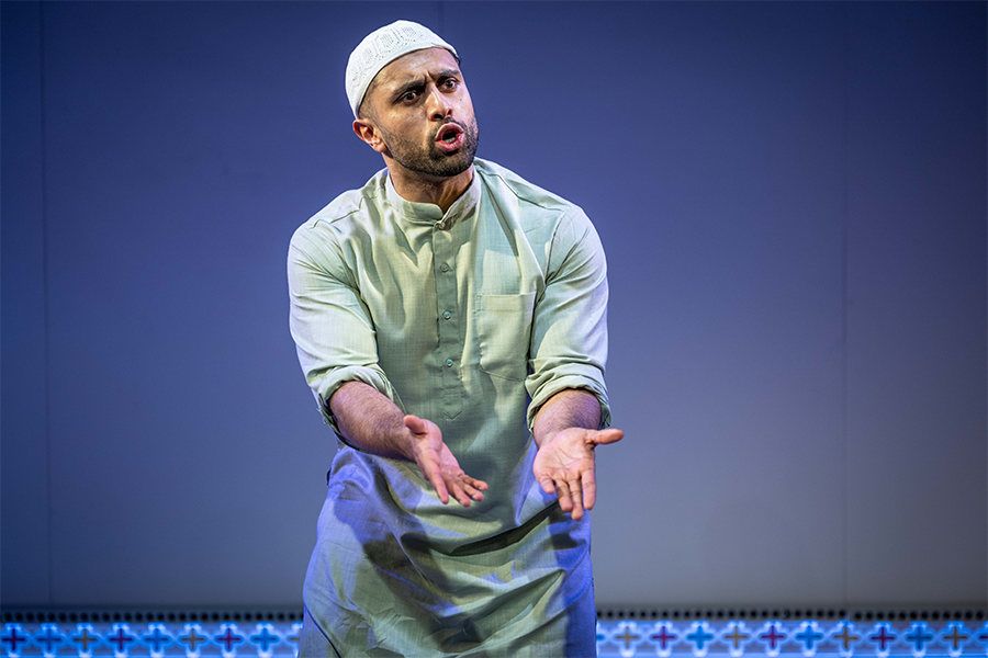 Azan Ahmed, a young south asian man, wears a Kurta and a Taqiyah. He gestures with his hands directed towards the floor.