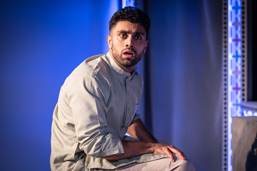 Azan Ahmed, a young south asian man, wears a Kurta and holds his mouth open shocked. The lighting is blue.