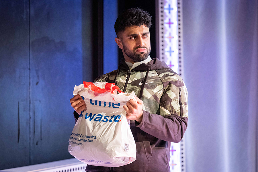 Azan Ahmed, a young south asian man, wears a nike camouflage hoodie and looks disgusted as he holds a plastic Tesco bag.